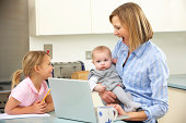 Mother with children using laptop in kitchen looking at each other smiling