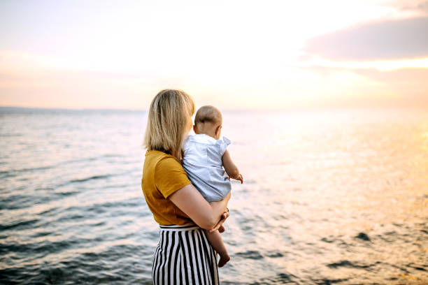 Mother with cute little baby girl enjoying sunset on the beach stock photo