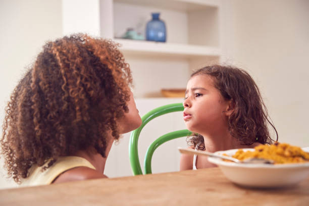 Mother With Daughter Who Is Fussy Eater Sitting Around Table At Home For Family Meal stock photo