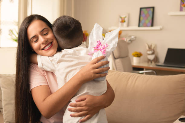 mother with easter egg hugging boy Happy cheerful brazilian mother with white easter egg hugging boy for the present in the couch easter sunday stock pictures, royalty-free photos & images