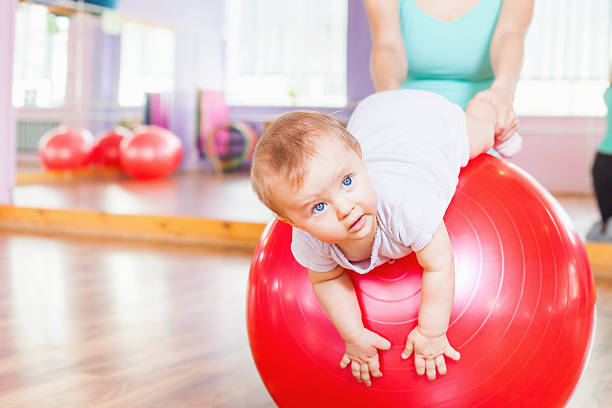 Mother with happy baby doing exercises with gymnastic ball stock photo
