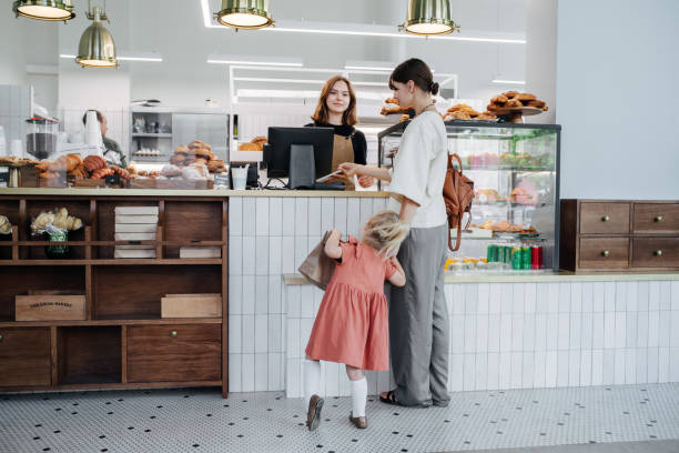 Mother with her daughter paying for pastry in a bakery shop. stock photo