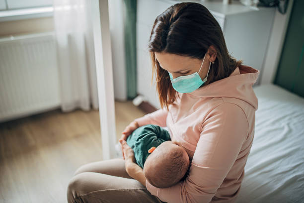 madre con maschera protettiva che allatta il figlio a casa - allattamento foto e immagini stock