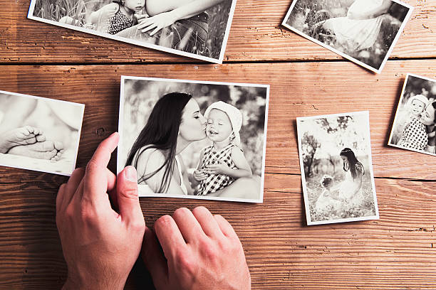 Mothers day composition. Black-and-white pictures, wooden backgr Mothers day composition. Hands of unrecognizable man holding  black-and-white photo. Studio shot on wooden background. holding photos stock pictures, royalty-free photos & images