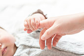 明るい部屋で赤ちゃんの手を握る母親の手