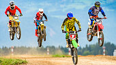 Four motocross racers in mid-air during a jump on a race track.