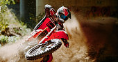 Motorsport photograph of a motocross rider in red sportswear riding his motorcycle on a dirt track in forest