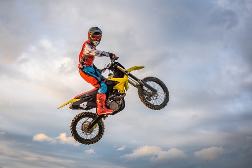 Motocross rider jumping mid air against cloudy sky.
