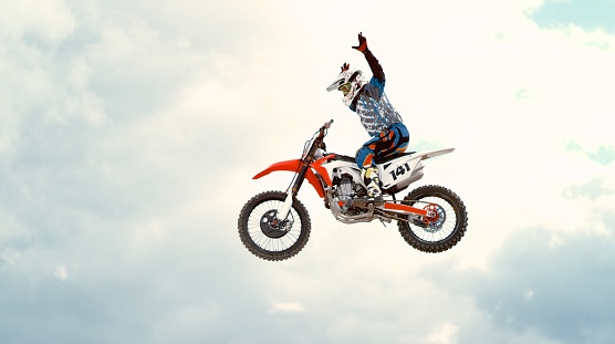Motocross rider performing stunt in mid-air against cloudy sky.