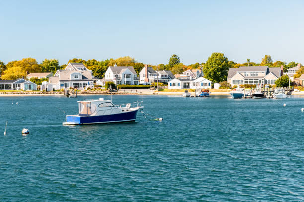 Motorboat moored off a built up coast on a sunny autumn day Empty boat anchored off a stretch of coast lined with residential buildings with private wooden jetties. Hyannis, Cape Cod, MA, USA. cape cod stock pictures, royalty-free photos & images