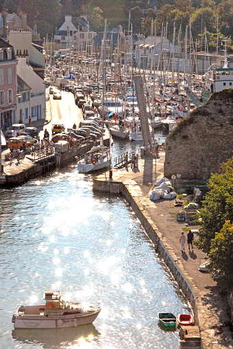 A motorboat waits outside the town quayside for space in the harbour marina, viewed overhead from the fortified ramparts of the castle, Sauzon, Belle Isle, Brittany, France. Belle-Île lies off the coast of the Gulf of Morbihan and is Brittany’s largest island. After a turbulent past, which included occupation by the British, the ‘beautiful isle’ is now a magnet for tourists, many of whom arrive by yacht or motorboat. France enjoys many quaint and historic towns and villages both coastal, on its islands and inland with beautiful architecture and historic detail such as stone carving, half timbered building construction and cobbled streets