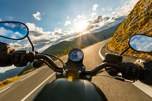 Motorcycle driver riding in Alpine highway, handlebars view, Austria, Europe.