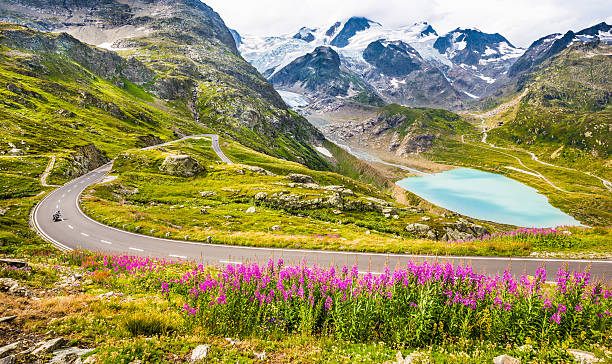 Motorcyclist on mountain pass road in the Alps Beautiful view of motorcyclist driving on winding mountain pass road in the Alps through gorgeous scenery with mountain peaks, glaciers, lakes and green pastures with blooming flowers in summer. wilderness area stock pictures, royalty-free photos & images