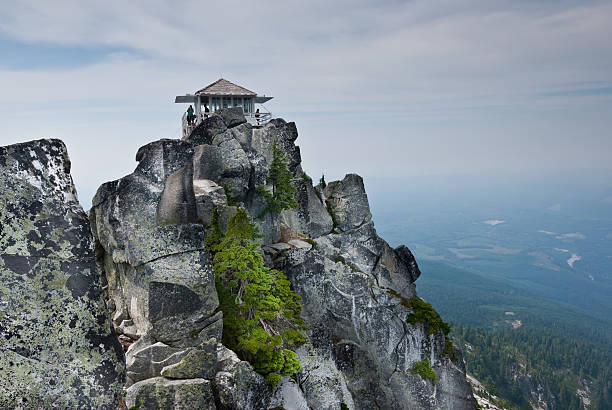 Mount Pilchuck Fire Lookout Mount Pilchuck State Park, Washington, USA - August 11, 2015: The historic Mount Pilchuck fire lookout was originally built in 1918 and rebuilt for visitor use in 1990. The lookout can be reached by hiking through beautiful old-growth forest and heather-covered meadows to the rocky summit.  There you can see an incredible panoramic view of the Puget Sound lowlands and the Cascade and Olympic Mountains.  These hikers were photographed standing on the fire lookout deck after reaching the 5341' summit of the mountain.  Mount Pilchuck is near Granite Falls, Washington State, USA. jeff goulden fire lookout stock pictures, royalty-free photos & images