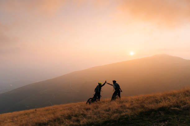 Mountain bikers give high-five at sunset Hazy valley behind holidays and celebrations stock pictures, royalty-free photos & images