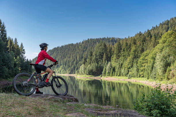 mountain biking in the black forest nice and ever young senior woman with her electric mountain bike at the Kinzig drinking Water reservoir in the northern Black Forest, Baden-Wuerttemberg, Germany electric bike workout stock pictures, royalty-free photos & images