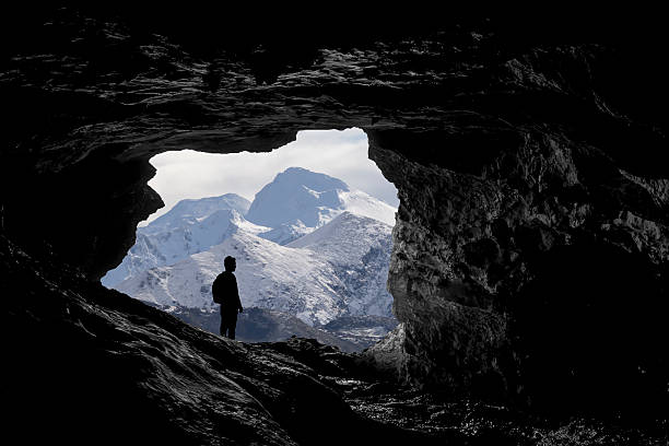 Mountain views Alone traveller into a cave viewing a snowy mountain landscape, Travel photography cave photos stock pictures, royalty-free photos & images