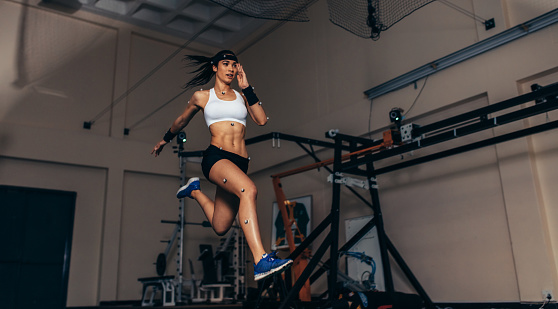 Female athlete with motion capture sensors on her body running in biomechanical lab. Recording the movement and performance of sportswoman in sports science lab.