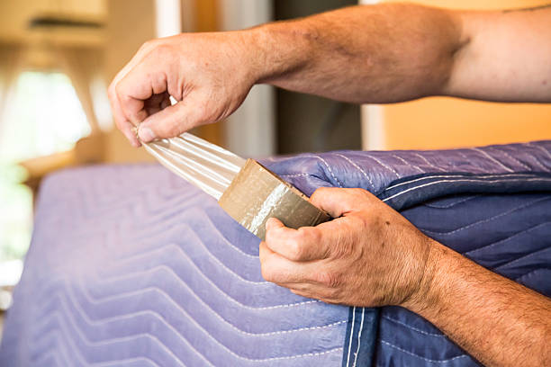 A mover tapes a padded blanket around a piece of furniture before transporting it.