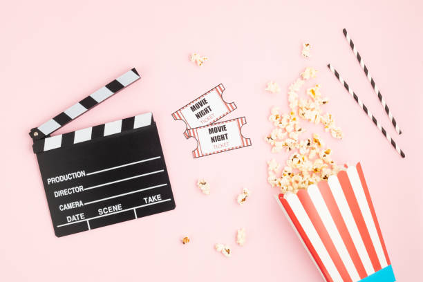 Movie clapperboard, tickets and popcorn over pink background. Movie night, home cinema, party invitation stock photo