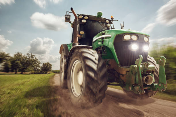 Moving Tractor on a dirt road Green tractor in full speed on a gravel road beside a field. tractor stock pictures, royalty-free photos & images
