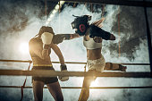 Female kick boxer jumping and hitting her opponent during the match in health club.