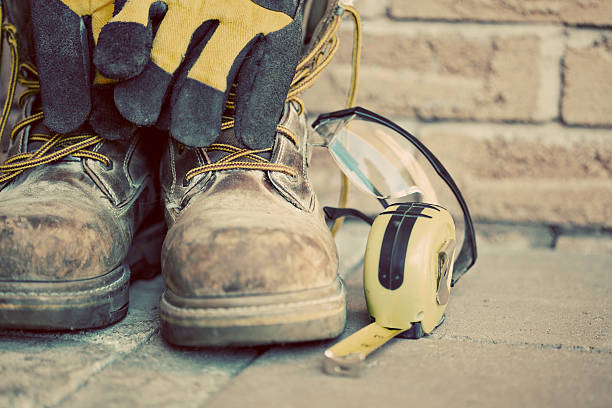 Muddy construction work boots with gloves and tape measure stock photo