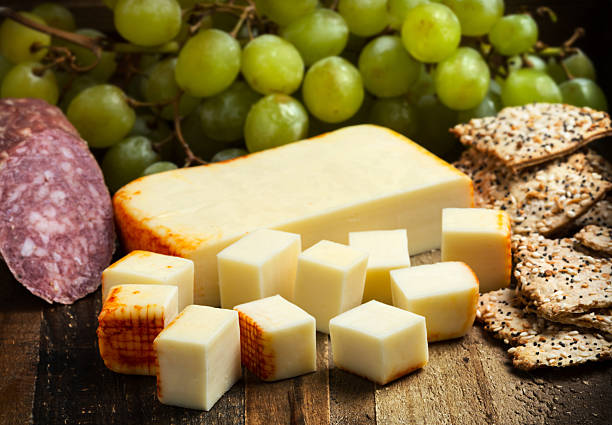 Muenster Cheese Muenster Cheese, salami, grapes and crackers over a wooden table muenster cheese stock pictures, royalty-free photos & images
