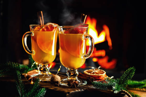 Mulled cider glasses on the background of fireplace fire. Hot mulled spiced apple cider cocktail for winter or autumn time. stock photo
