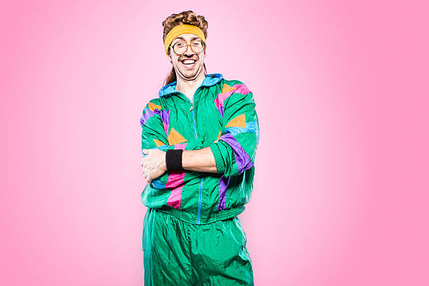 Mullet Man With Eighties Fashion Style A cool, funky young adult in late 1980's / early 1990's fashion style, with mullet, fluorescent colored track suit, nerdy glasses, and sweat band.  He smiles at the camera with a cheesy grin, his arms folded. Vibrant pink background. Horizontal with copy space. mullet haircut photos stock pictures, royalty-free photos & images