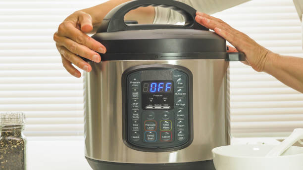 Multi cooker close up on kitchen table. Woman lifting the lid stock photo