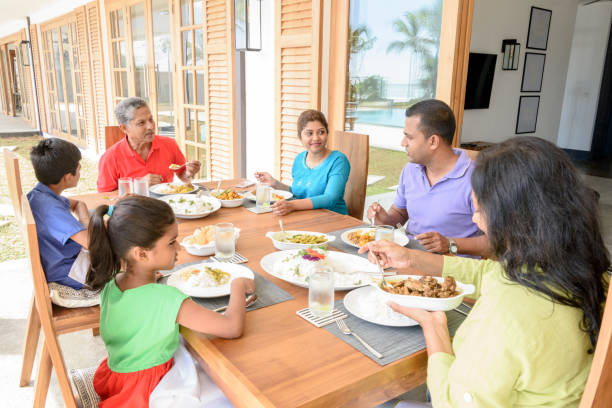Multi generation family having dinner together Two children with their parents and grandparents enjoying a meal, sitting at dining table with plates of food and serving dishes asian family eating together stock pictures, royalty-free photos & images
