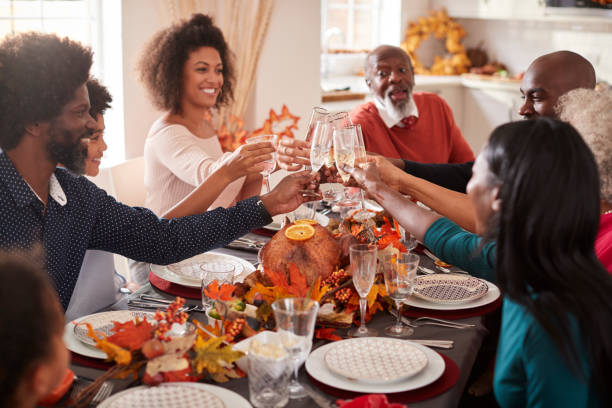 multi generation blandad ras familj höja sina glasögon för att göra en toast på sin thanksgiving middag tabell - family dinner bildbanksfoton och bilder
