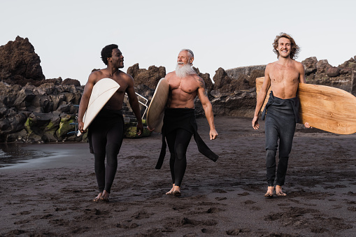 Multi generational surfer men having fun walking by the beach - Main focus on senior face