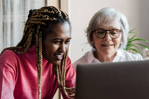 Multi generational women having video call with colleagues using computer app - Multiracial people using laptop computer - Elderly enjoying technology concept - Focus on senior face stock photo