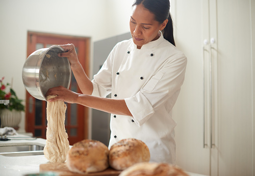 fresh handmade dough. Mature woman kneading dough in modern kitchen at home, senior female wearing chef coat cooking homemade pastry cookies, bread or pie, using fresh natural products flour eggs, standing at wooden desk