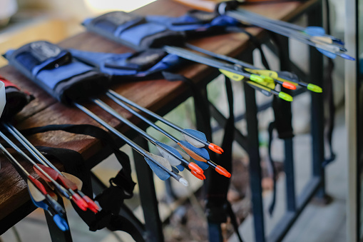 Close-up shot group of multi-colored arrows inside their quivers lying on a table at an archery range.