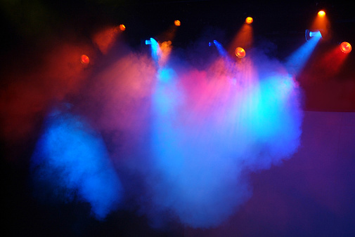 Horizontal image of dramatic stage lights with fog creating clouds of blue and red. Approximately ten red and blue stage spot lights are shinning from above the stage. The support framework of the lights is not visible. They are shinning onto an empty stage.