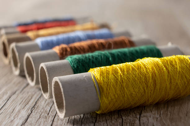 multi-colored threads on a light wooden background. threads for sewing in a row on the table. - linha artigo de costura imagens e fotografias de stock