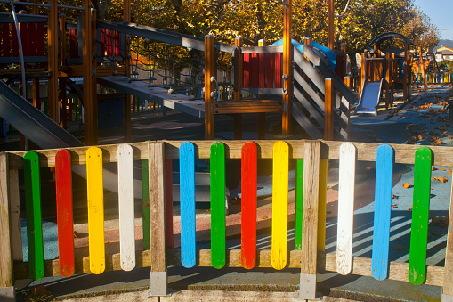 Multicolored wooden fence  surrounding a children playground at dusk, close-up front wide angle view. Galicia, Spain.
