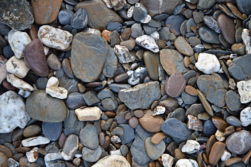 A horizontal photograph of a ground  of Pebbles, in different sizes and shades of Grey(gray), brown. The background is bright, has no people and no text.