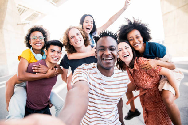 Multicultural happy friends having fun taking group selfie portrait on city street - Young diverse people celebrating laughing together outdoors - Happy lifestyle concept stock photo