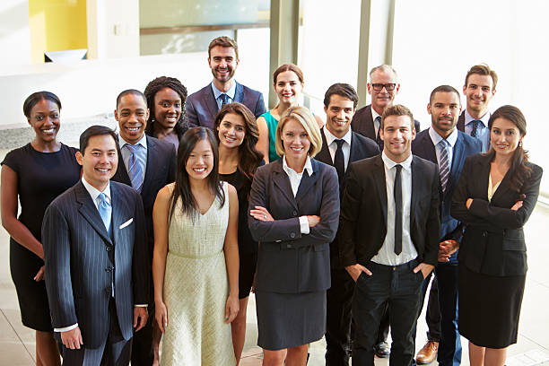 Multi-cultural office staff standing in lobby Portrait Of Multi-Cultural Office Staff Standing In Lobby Smiling At Camera businesswear stock pictures, royalty-free photos & images
