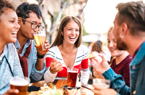 Multicultural people drinking beer at brewery bar garden - Genuine friendship life style concept with men and women spending happy hour together at open air pub dehor - Warm vivid backlight filter stock photo