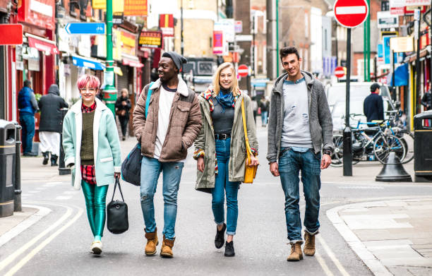 Multicultural students walking on Brick Lane center at Shoreditch London - Life style concept with multi-ethnic young friends on seasonal clothes having fun together outside - Bright vivid filter stock photo