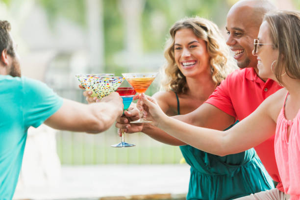 Multi-ethnic adults at party with cocktails, toasting A multi-ethnic group of adult friends at an outdoor party, drinking cocktails. An interracial mid adult couple and a young caucasian woman are toasting with a young man. The focus is on the mixed race black and hispanic man. margarita toast stock pictures, royalty-free photos & images