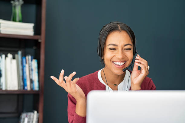 multiethnic businesswoman talking and laughing over headphone during video call - trabalhar a partir de casa imagens e fotografias de stock