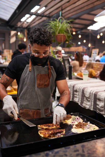 A multi-ethnic chef folds over tacos on the grill at a busy food market stock photo