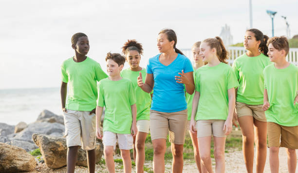 Multi-ethnic children, teacher, field trip by ocean A group of multi-ethnic children and their teacher on a field trip to a marine park. They are walking along a beach covered with boulders. The teacher, a Pacific Islander woman in her 30s, is in the middle, talking to her students Camp Counselor stock pictures, royalty-free photos & images