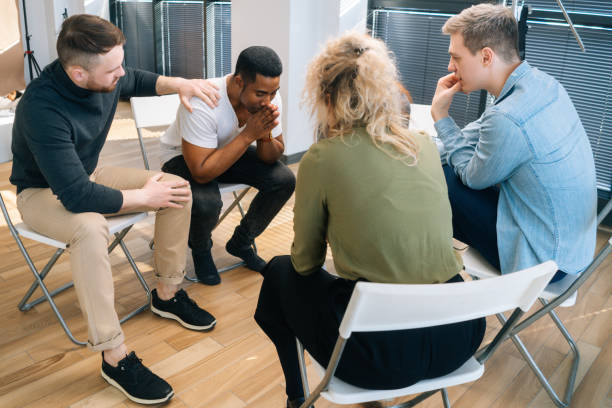 Multiethnic diverse people supporting depressed African American young male during group therapy session. stock photo